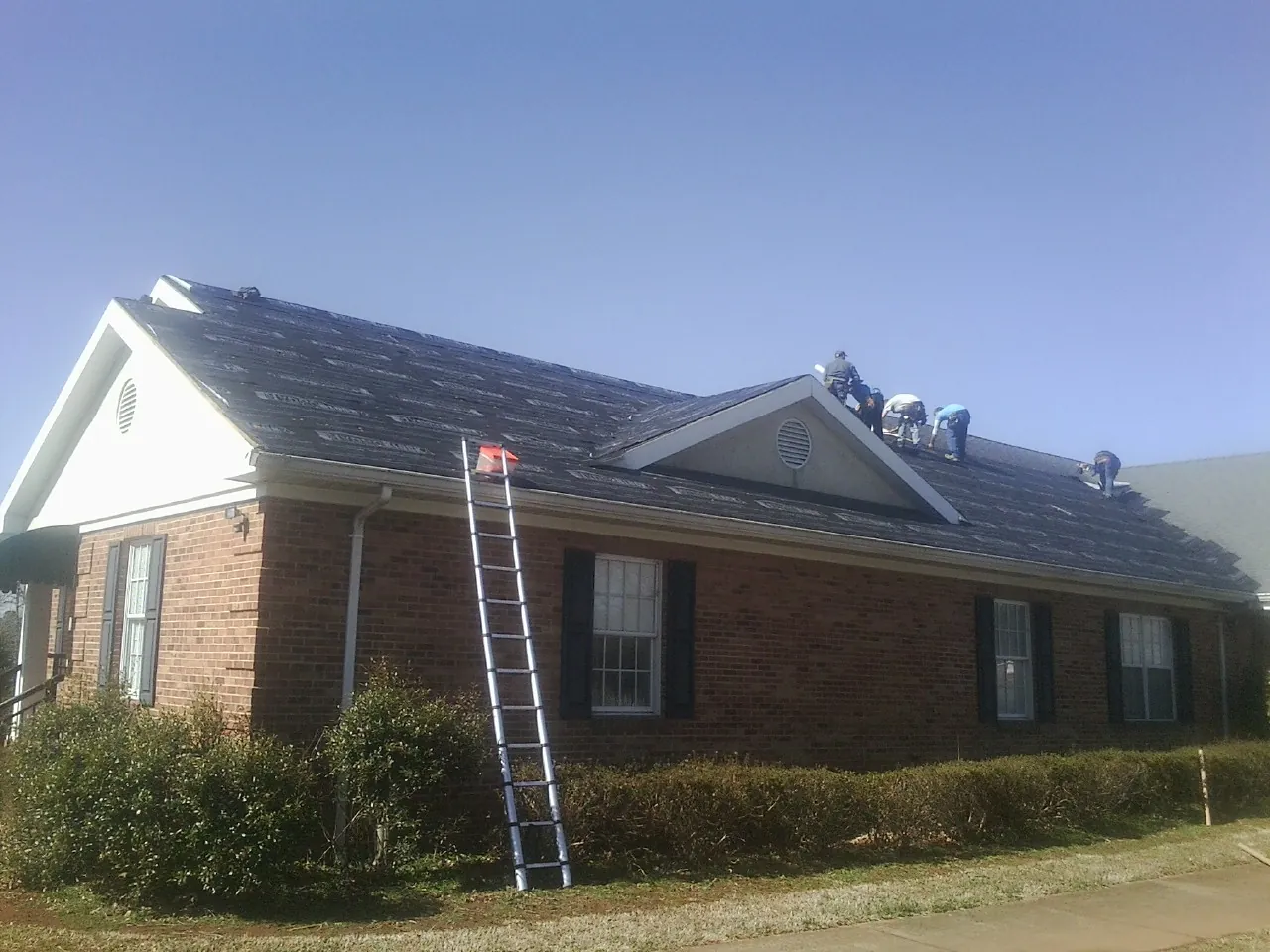 Crew tearing shingles off a brick ranch roof with a ladder set — Emergency Roof Repair work by our crew in Mount Sherman