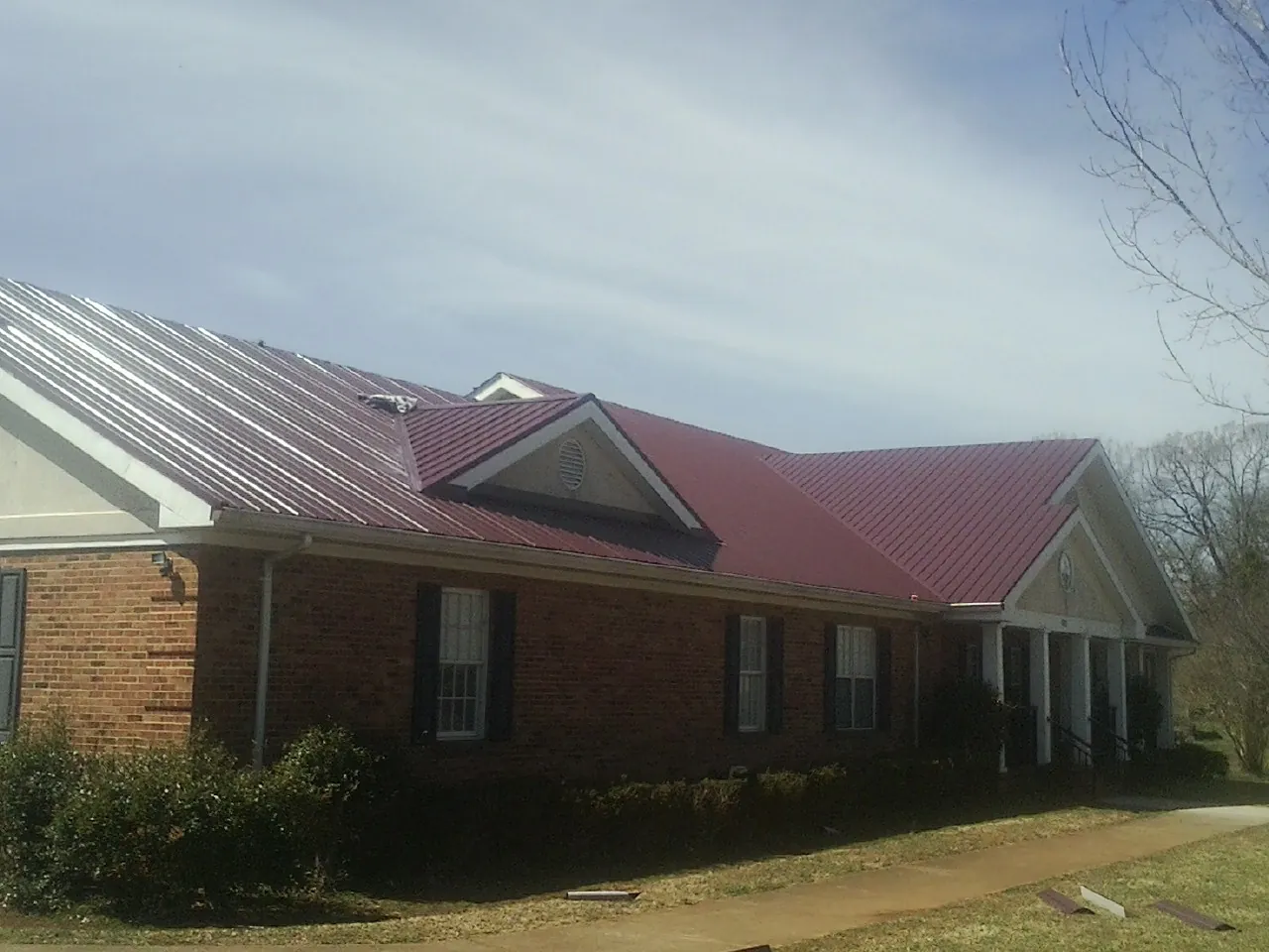 Red metal roof with gabled entries on a long brick building, from a Hail Damage Roof Repair job in Mount Sherman