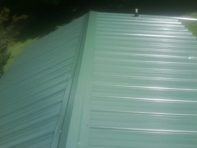 New green metal panels meeting at the ridge of a roof — Flat Roof Repair work by our crew in Mount Sherman