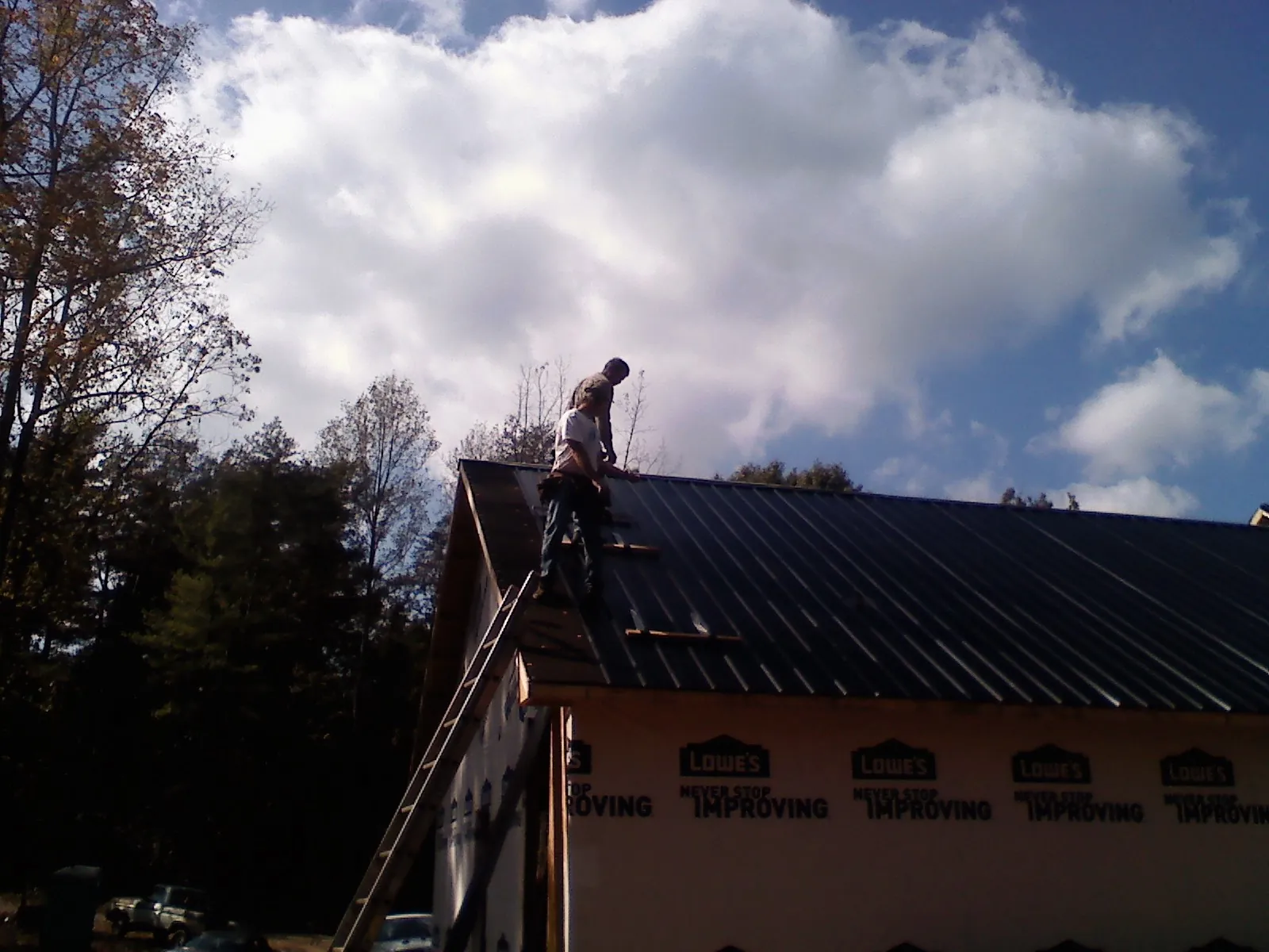 Roofer fastening dark metal panels high against a cloudy sky, from a Roof Inspection job in Mount Sherman