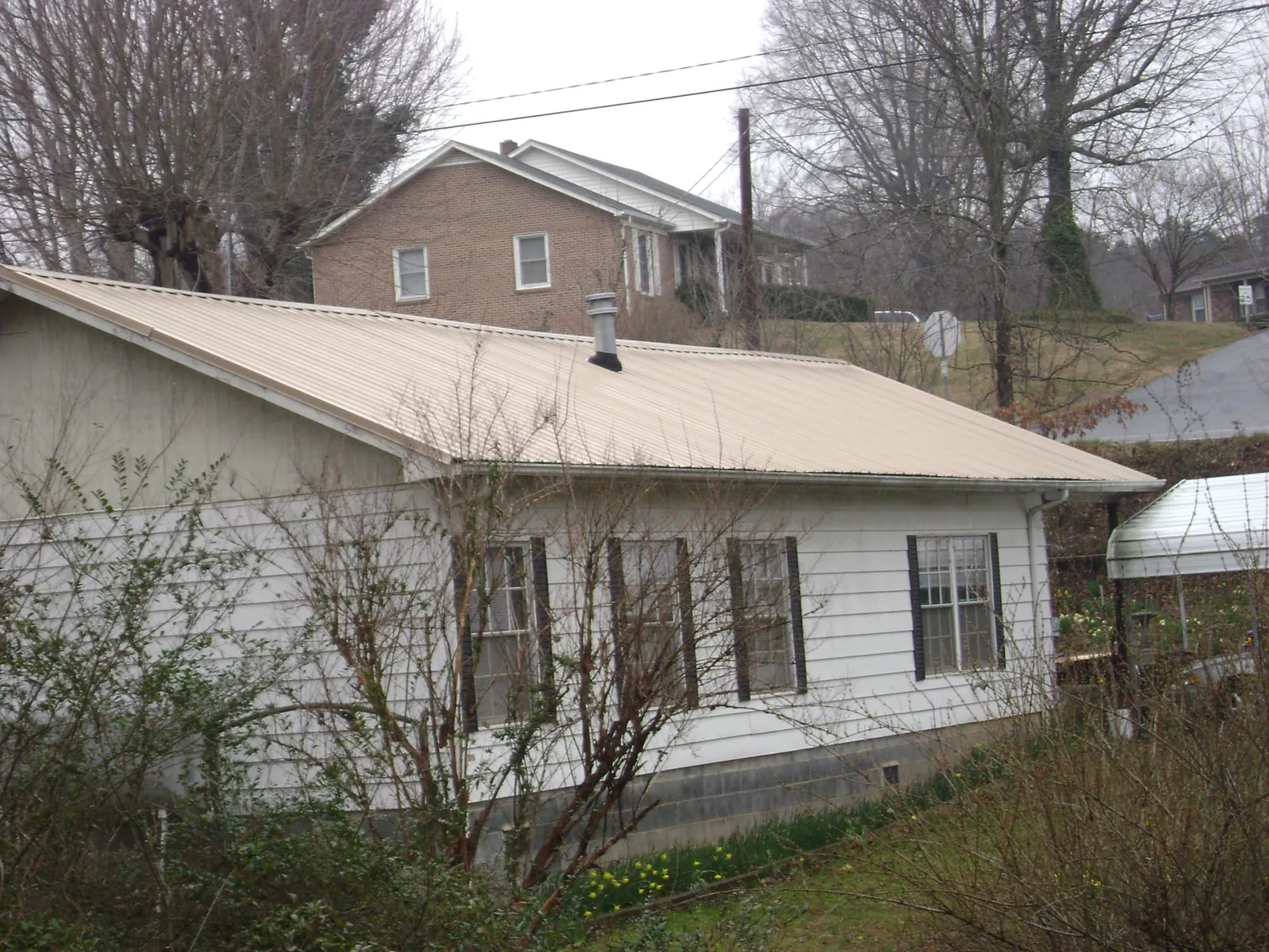 Tan metal roof on a white sided house set into a hillside — Commercial Roofing by Roofing Brothers in Mount Sherman